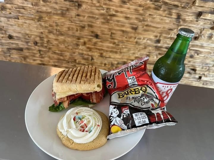 A pressed panini with chips, an Ale-8, and a frosted cookie on a plate