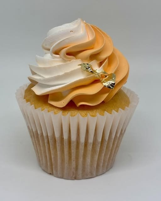 A gourmet Cupcake Apothecary cupcake with orange and white swirled buttercream and a gold leaf accent