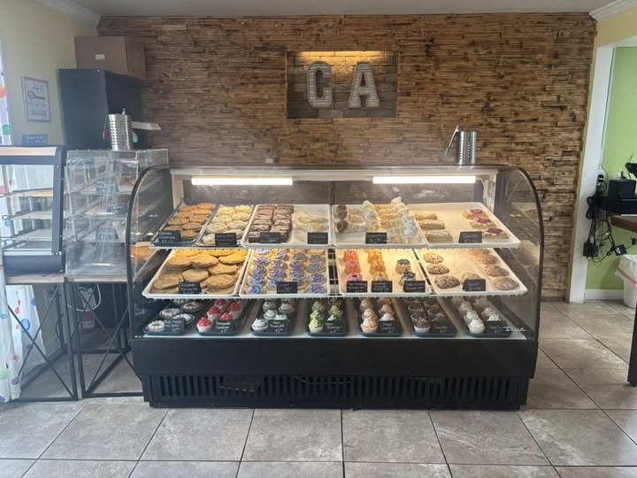 The Cupcake Apothecary display case filled with fresh cupcakes, bundts, and pastries against a rustic wood wall